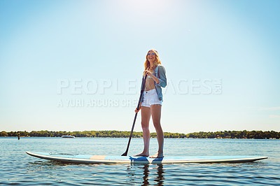 Buy stock photo Shot of an attractive young woman paddle boarding on a lake