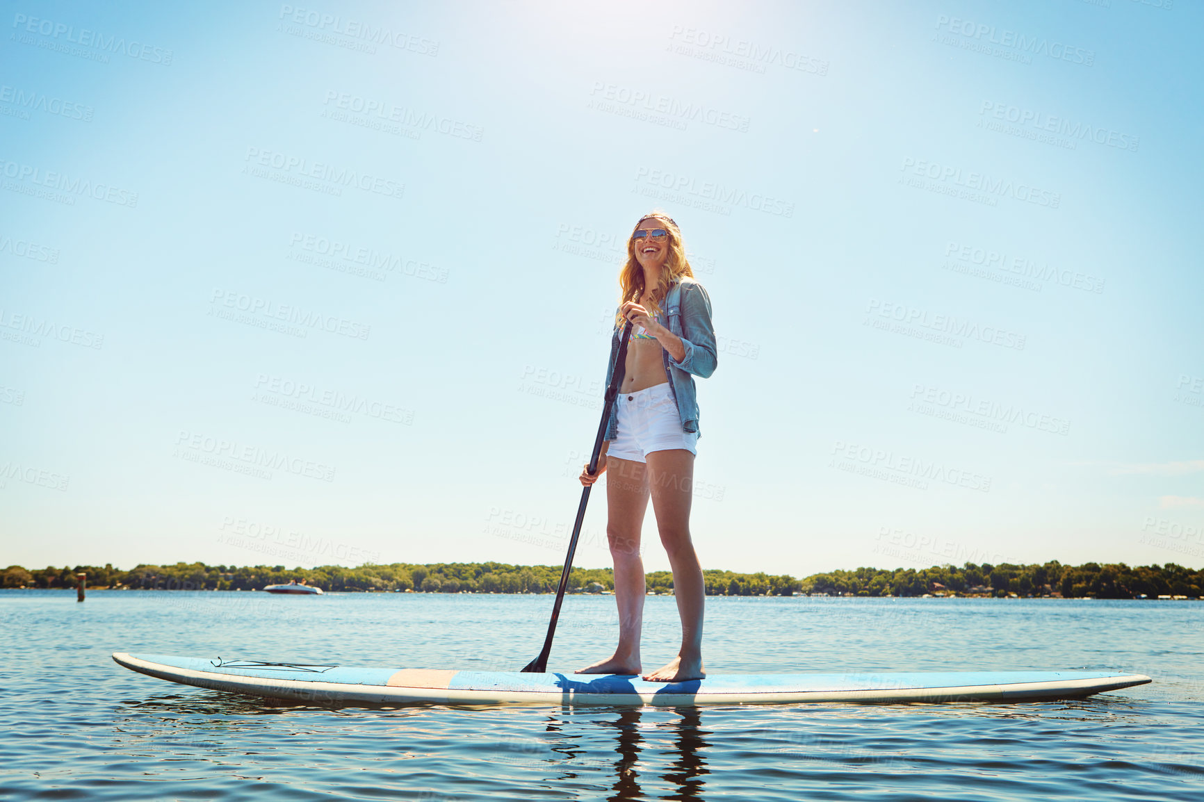 Buy stock photo Shot of an attractive young woman paddle boarding on a lake