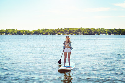 Buy stock photo Shot of an attractive young woman paddle boarding on a lake