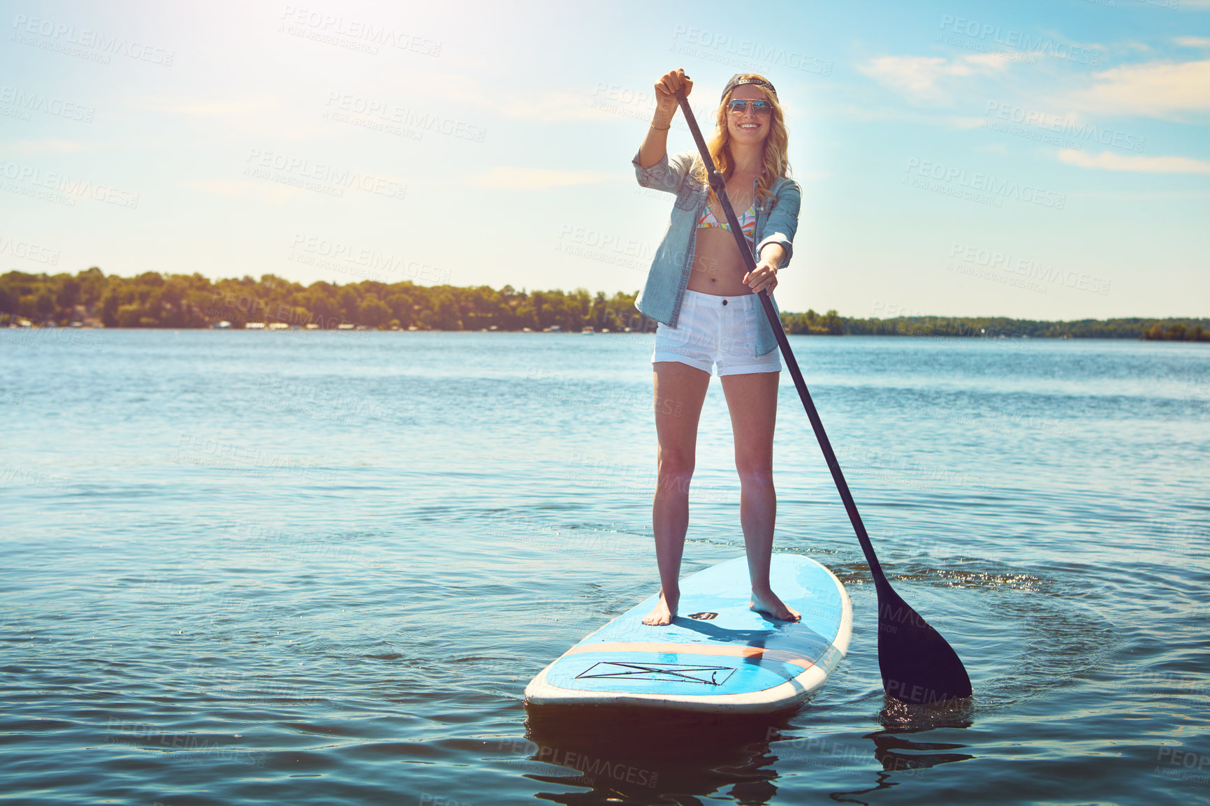 Buy stock photo Shot of an attractive young woman paddle boarding on a lake