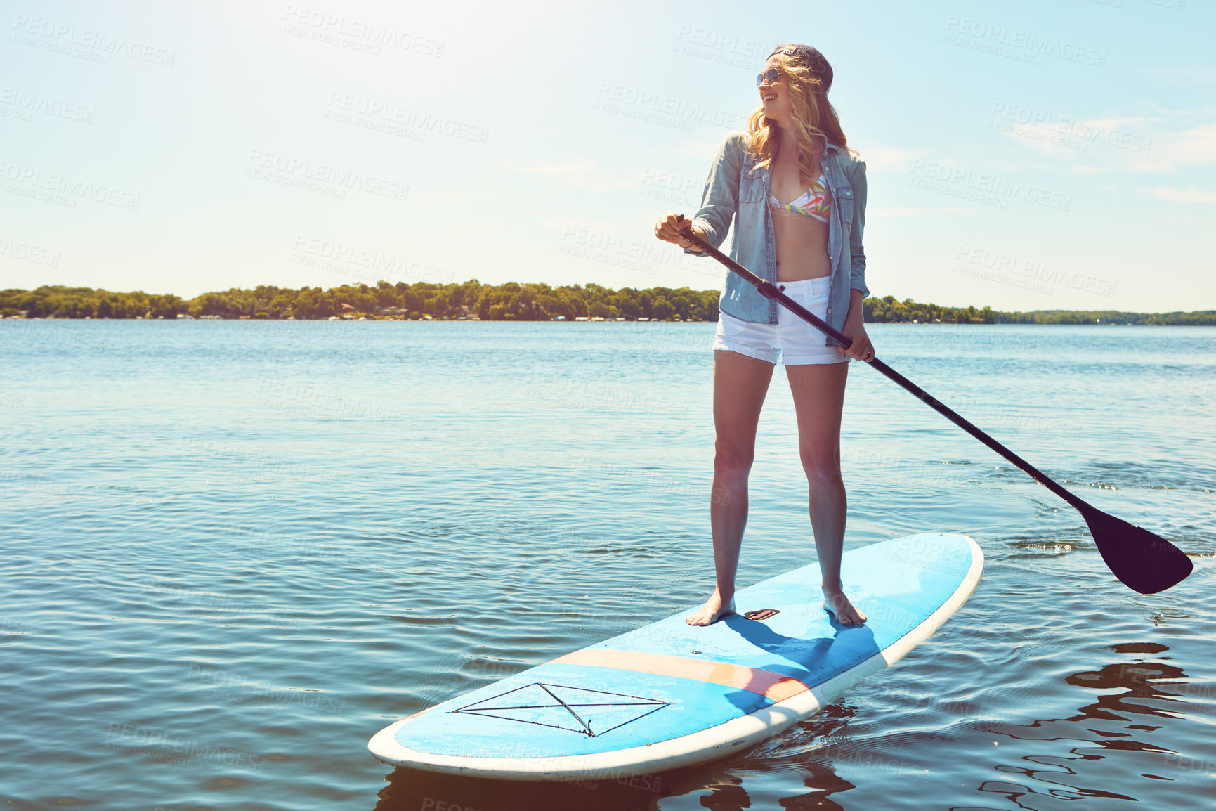 Buy stock photo Shot of an attractive young woman paddle boarding on a lake