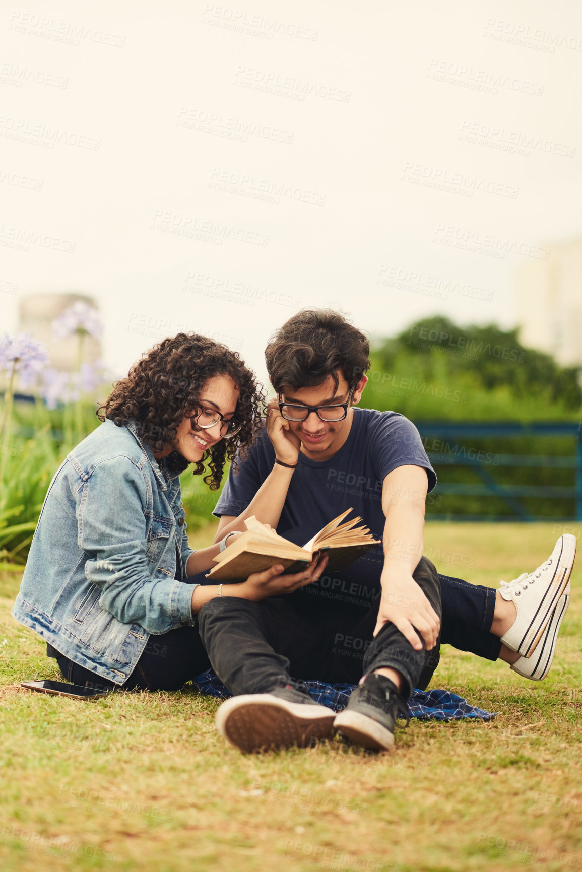 Buy stock photo Shot of a teenage couple reading a book together outdoors