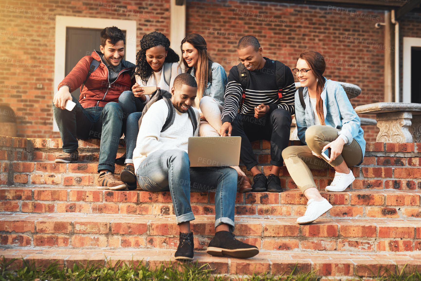 Buy stock photo Shot of a group of students using a laptop together on campus