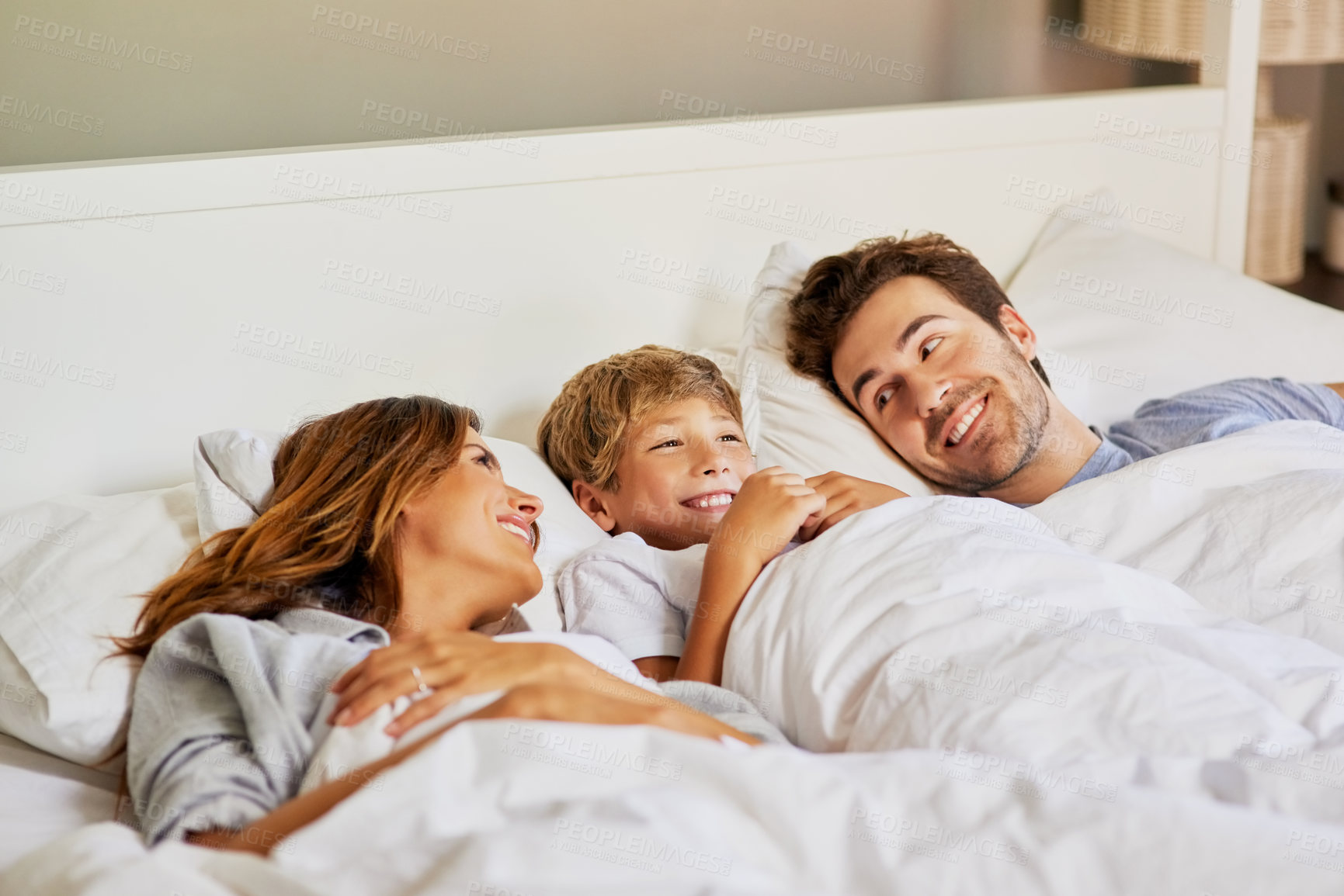 Buy stock photo Shot of a cheerful young family relaxing in bed at home during the day
