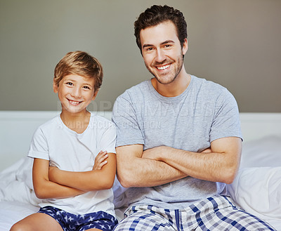 Buy stock photo Portrait of a cheerful father and son seated on a bed with arms folded while looking at the camera at home in the morning