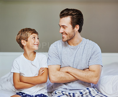 Buy stock photo Shot of a cheerful father and son seated on a bed with arms folded while looking at the camera at home in the morning