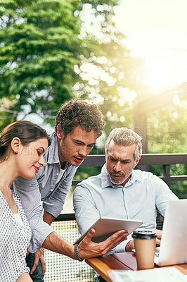 Buy stock photo Shot of a team of colleagues using a laptop and digital tablet together during a meeting outdoors