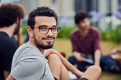 Buy stock photo Portrait of a cheerful young man  sitting in the park with his friends and studying outside during the day