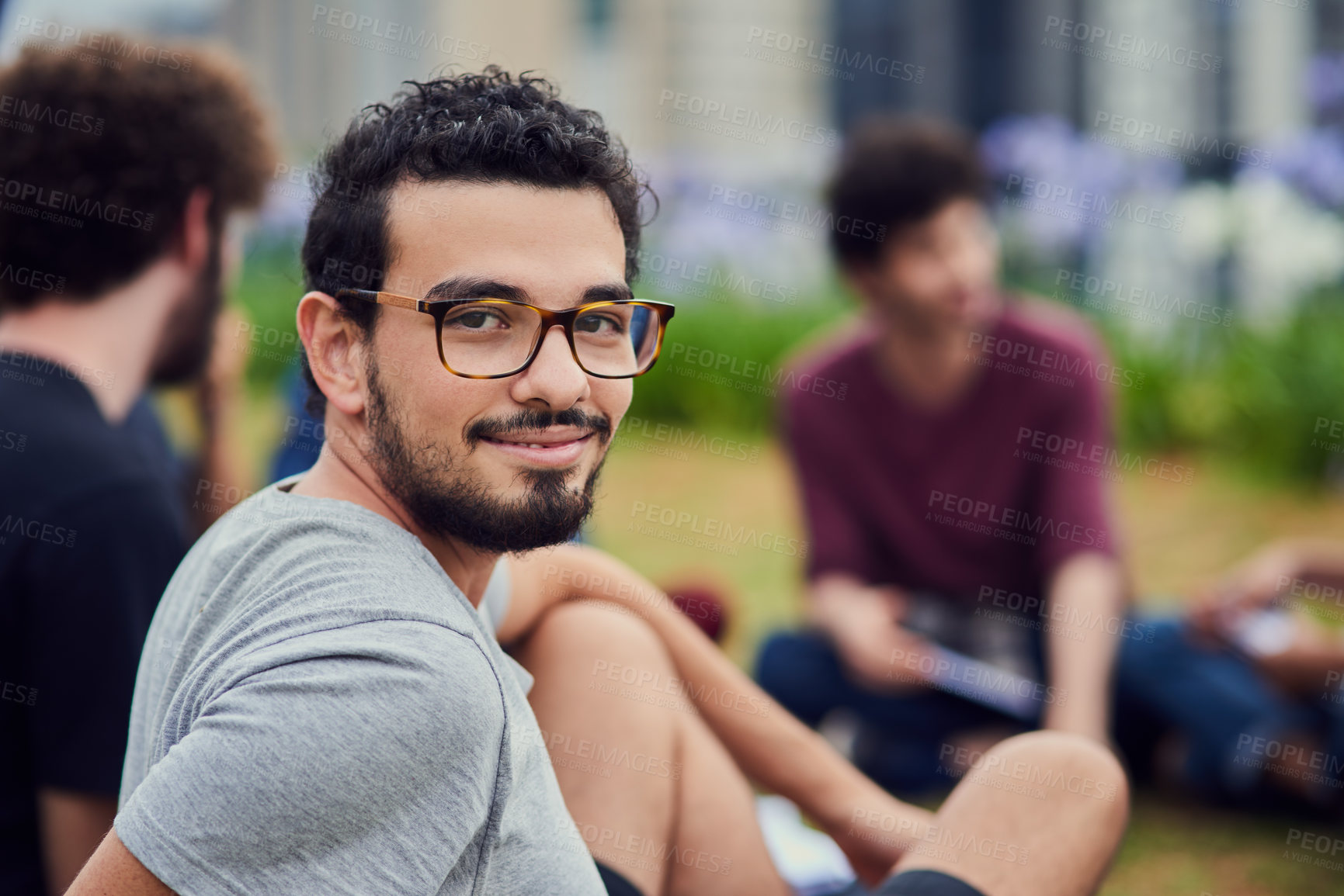Buy stock photo Portrait of a cheerful young man  sitting in the park with his friends and studying outside during the day