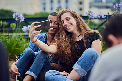 Buy stock photo Shot of two young friends taking a self portrait together while being seated in a park outside during the day
