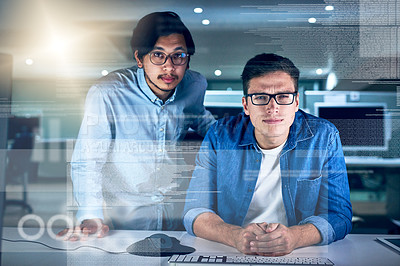 Buy stock photo Portrait of two young male programmers working on a computer together in the office at night