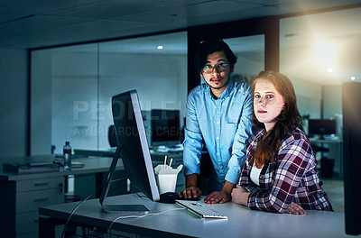Buy stock photo Portrait of two focussed young programmers working together on a computer in the office at work during the night