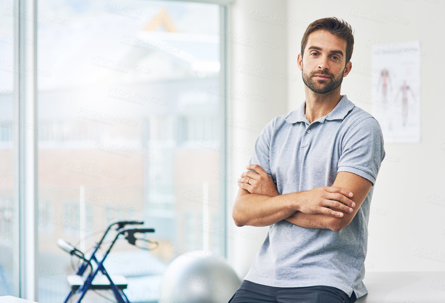 Buy stock photo Cropped portrait of a male physiotherapist sitting with his arms folded in his office