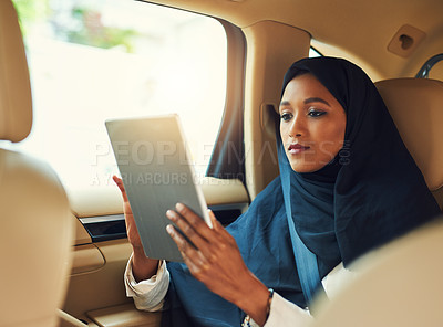 Buy stock photo Shot of a focussed young businesswoman browsing on a digital tablet while seated in the backseat of a car driving to work during the day