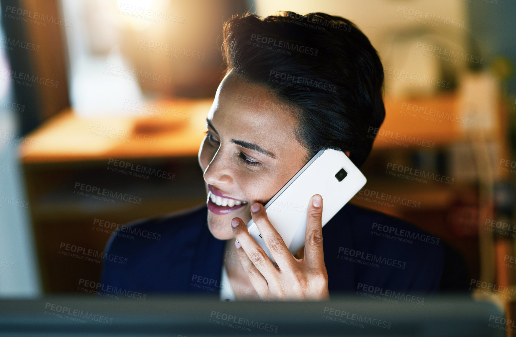 Buy stock photo Shot of a young businesswoman talking on a cellphone while working late in an office