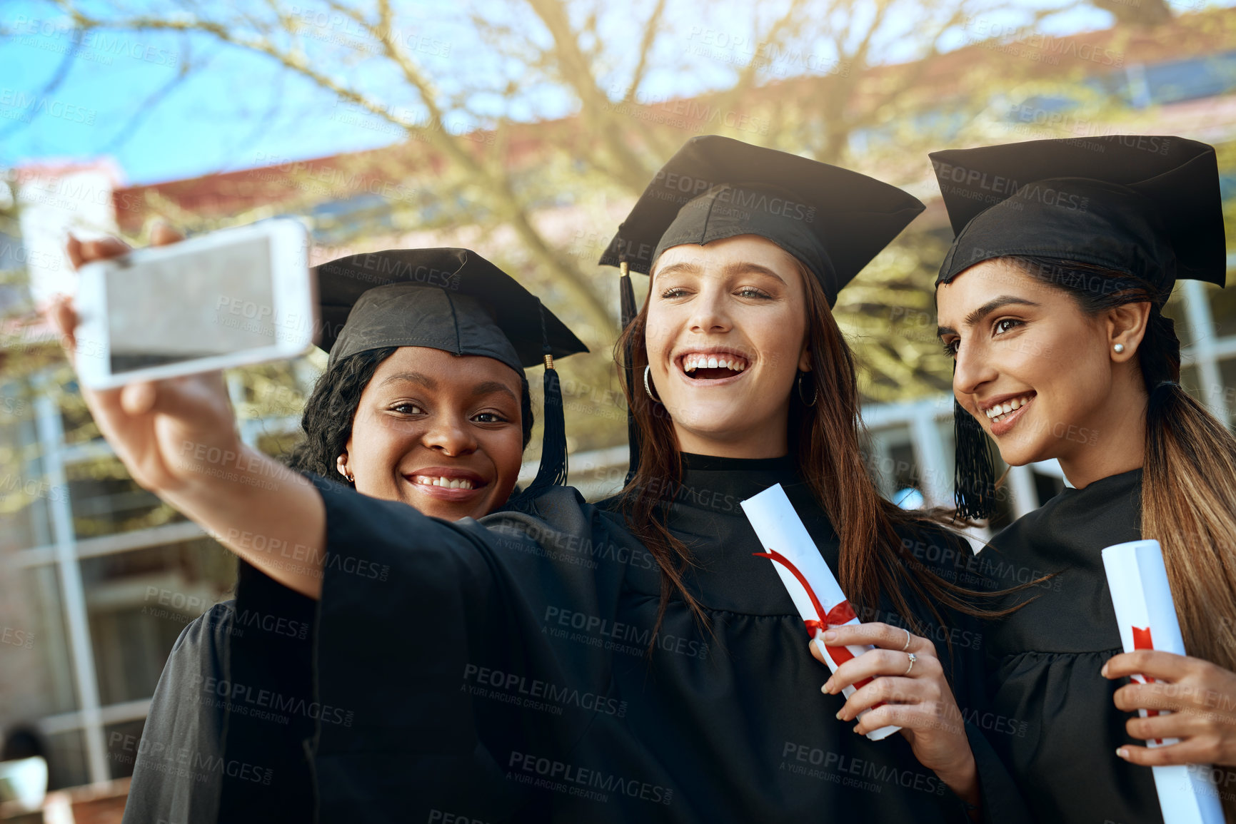 Buy stock photo Shot of a group of young women taking selfies with a mobile phone on graduation day