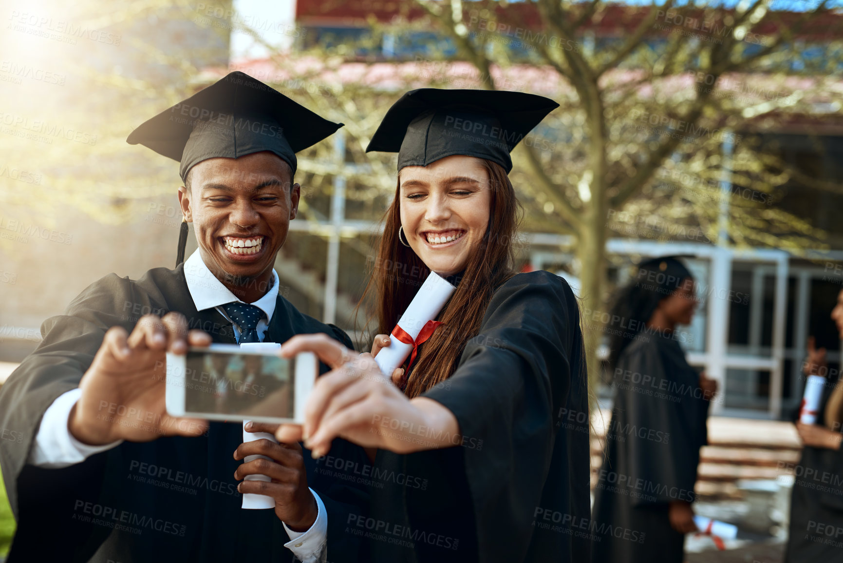 Buy stock photo Shot of a young man and woman taking selfies with a mobile phone on graduation day