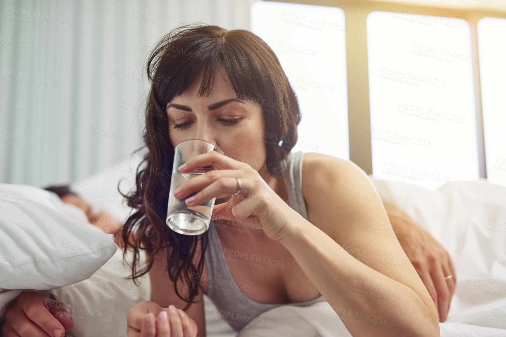 Buy stock photo Shot of a tired young woman waking up after sleeping and drinking water while still being in bed