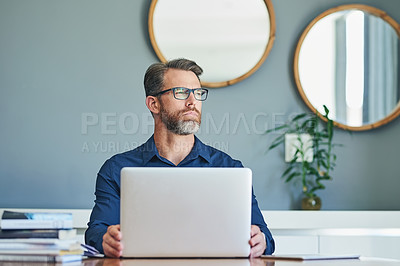Buy stock photo Shot of a confident middle aged businessman working on his laptop while looking into the distance and contemplating at home during the day