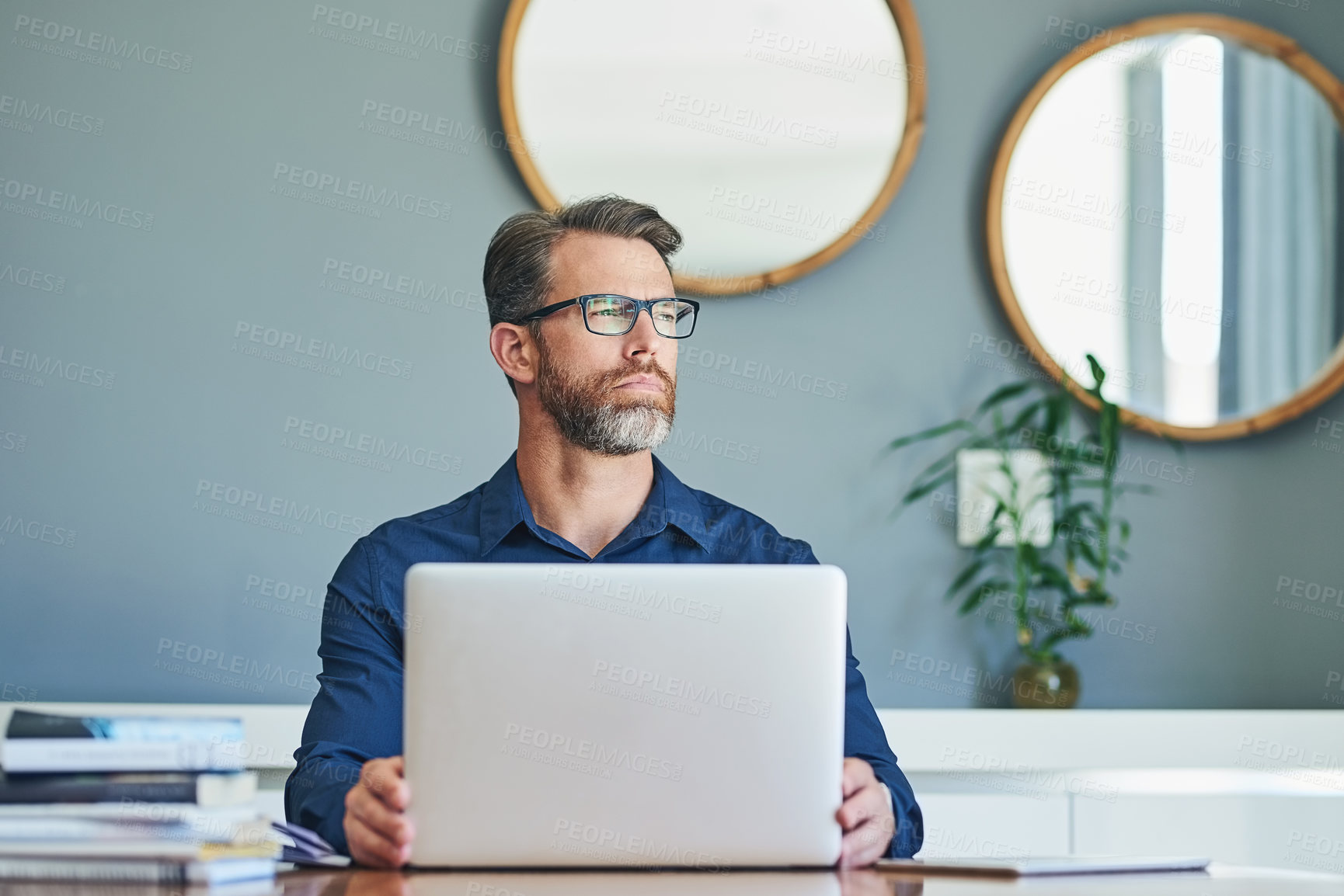 Buy stock photo Shot of a confident middle aged businessman working on his laptop while looking into the distance and contemplating at home during the day