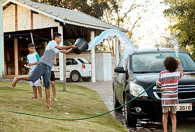 Buy stock photo Shot of a group of cheerful young kids washing their parent's car together outside during the day