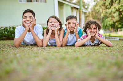 Buy stock photo Portrait of a group of happy siblings lying together on the grass in their backyard