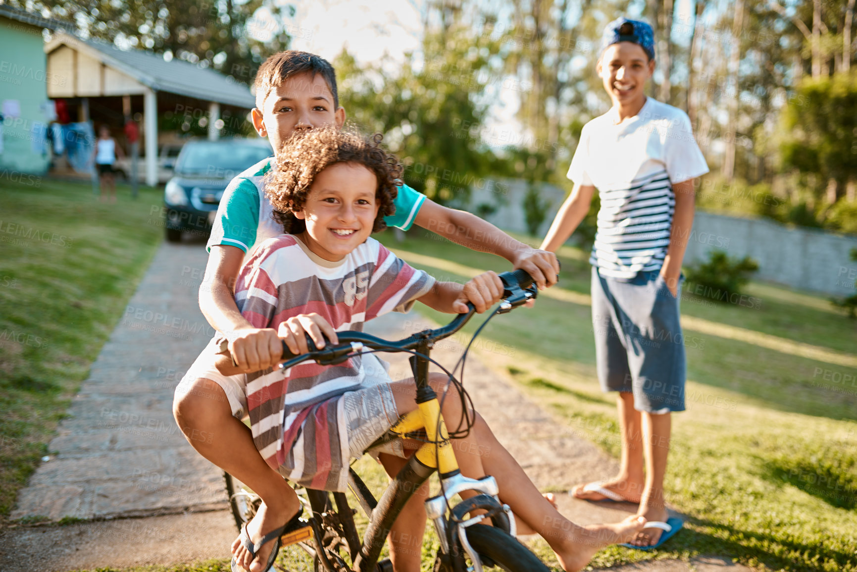 Buy stock photo Shot of happy young brothers riding a bicycle together in their backyard