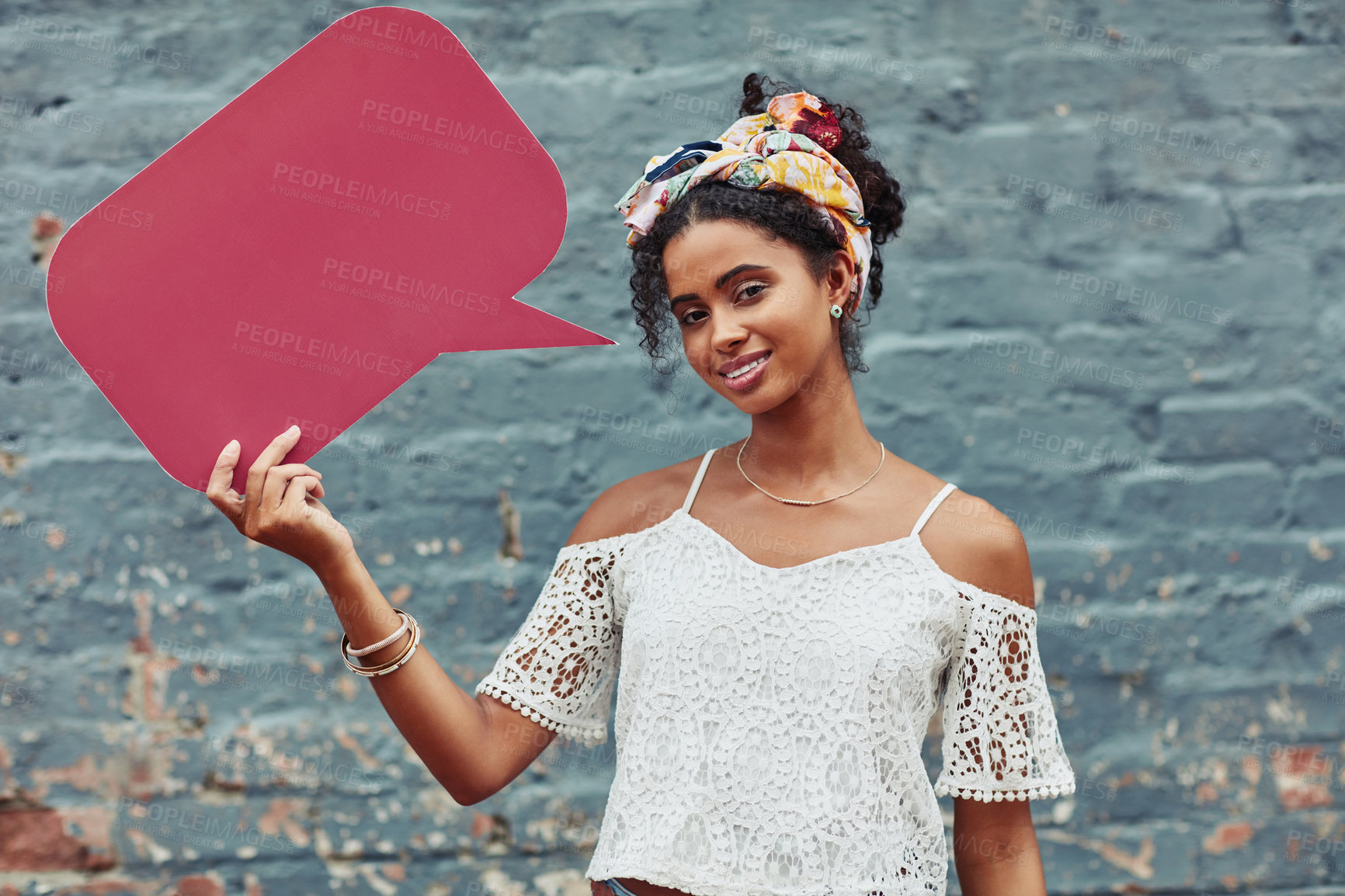 Buy stock photo Cropped shot of an attractive young woman holding a speech bubble against a brick wall outside
