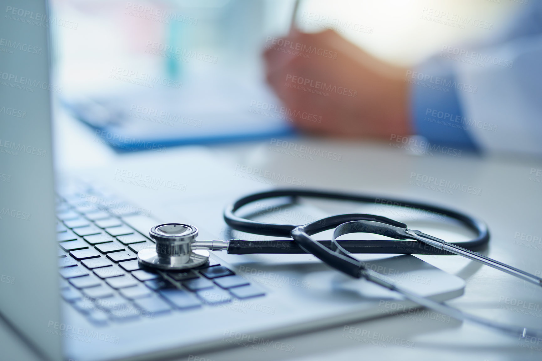 Buy stock photo Closeup shot of a stethoscope resting on a laptop with an unrecognizable doctor working in the background