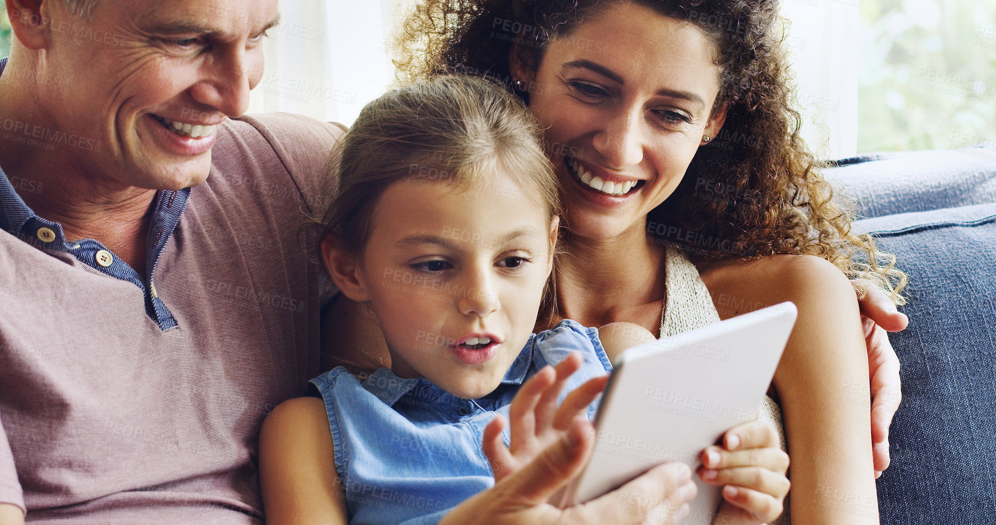 Buy stock photo Shot of a cute little girl using a digital tablet with her mother and father on the sofa at home