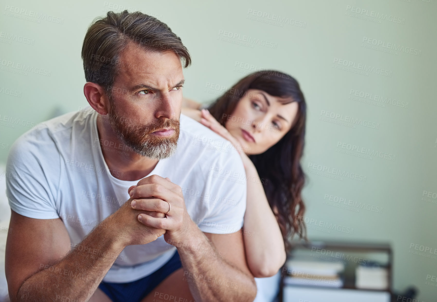 Buy stock photo Shot of a unhappy looking middle aged man looking into the distance while his partner tries to comfort him in the bedroom