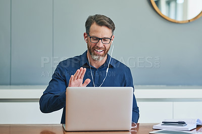 Buy stock photo Shot of a cheerful middle aged businessman making a Skype call on his laptop and waving to the screen at home during the day