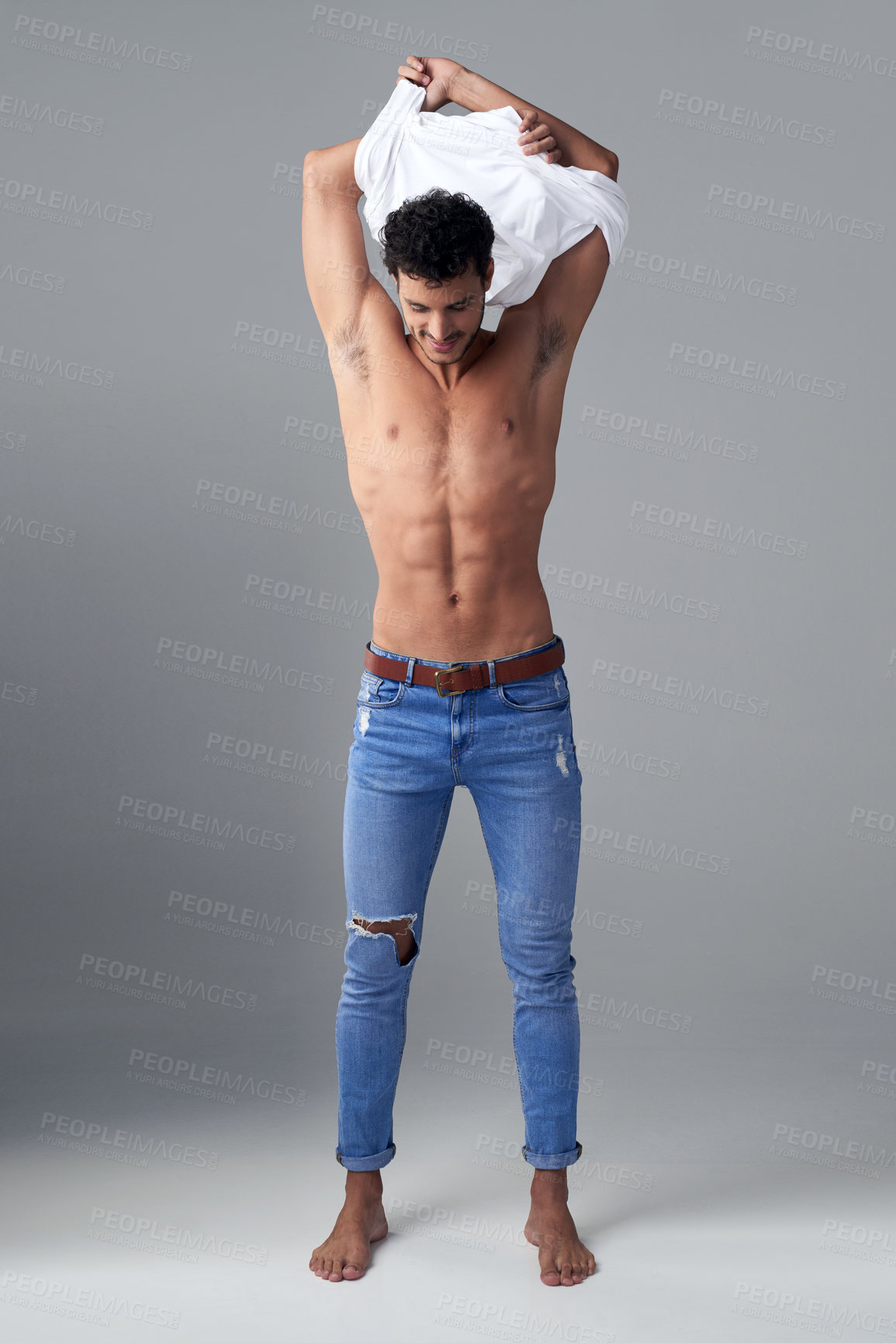 Buy stock photo Studio shot of a handsome young man undressing against a grey background