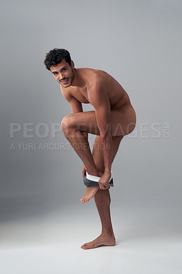 Buy stock photo Studio shot of a handsome young man undressing against a grey background