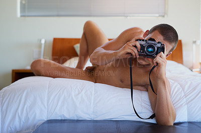 Buy stock photo Shot of a handsome shirtless young man taking a picture on his bed at home