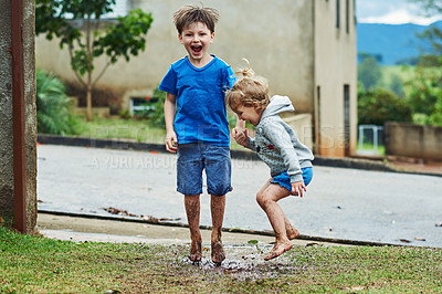 Buy stock photo Portrait of two cheerful young children jumping around in mud outside during a rainy day