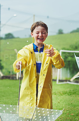 Buy stock photo Shot of a cheerful little boy standing with an umbrella while getting soaked with rain outside during the day