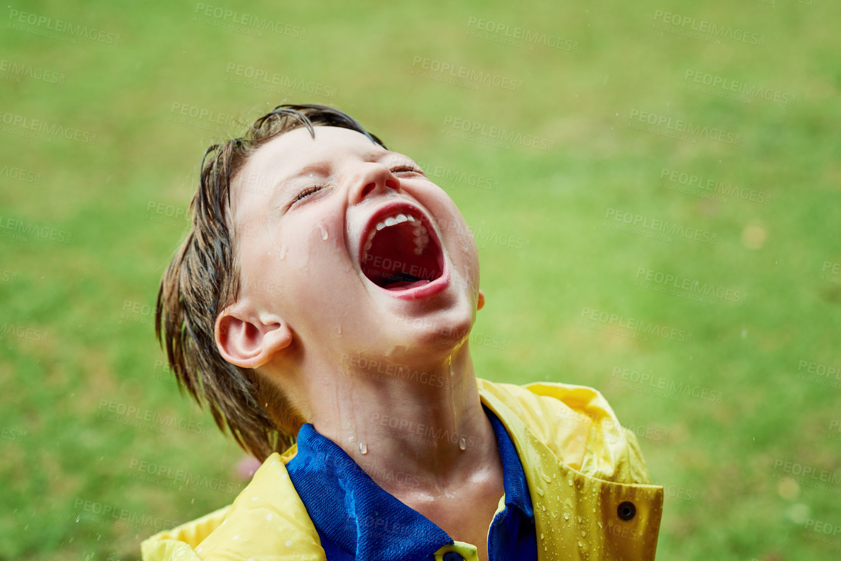 Buy stock photo Shot of a cheerful little boy standing on his own while opening his mouth to catch rain drops outside on a rainy day
