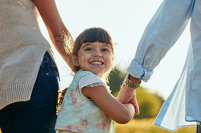 Buy stock photo Portrait of an adorable and happy little girl holding her mother and father’s hands in the park
