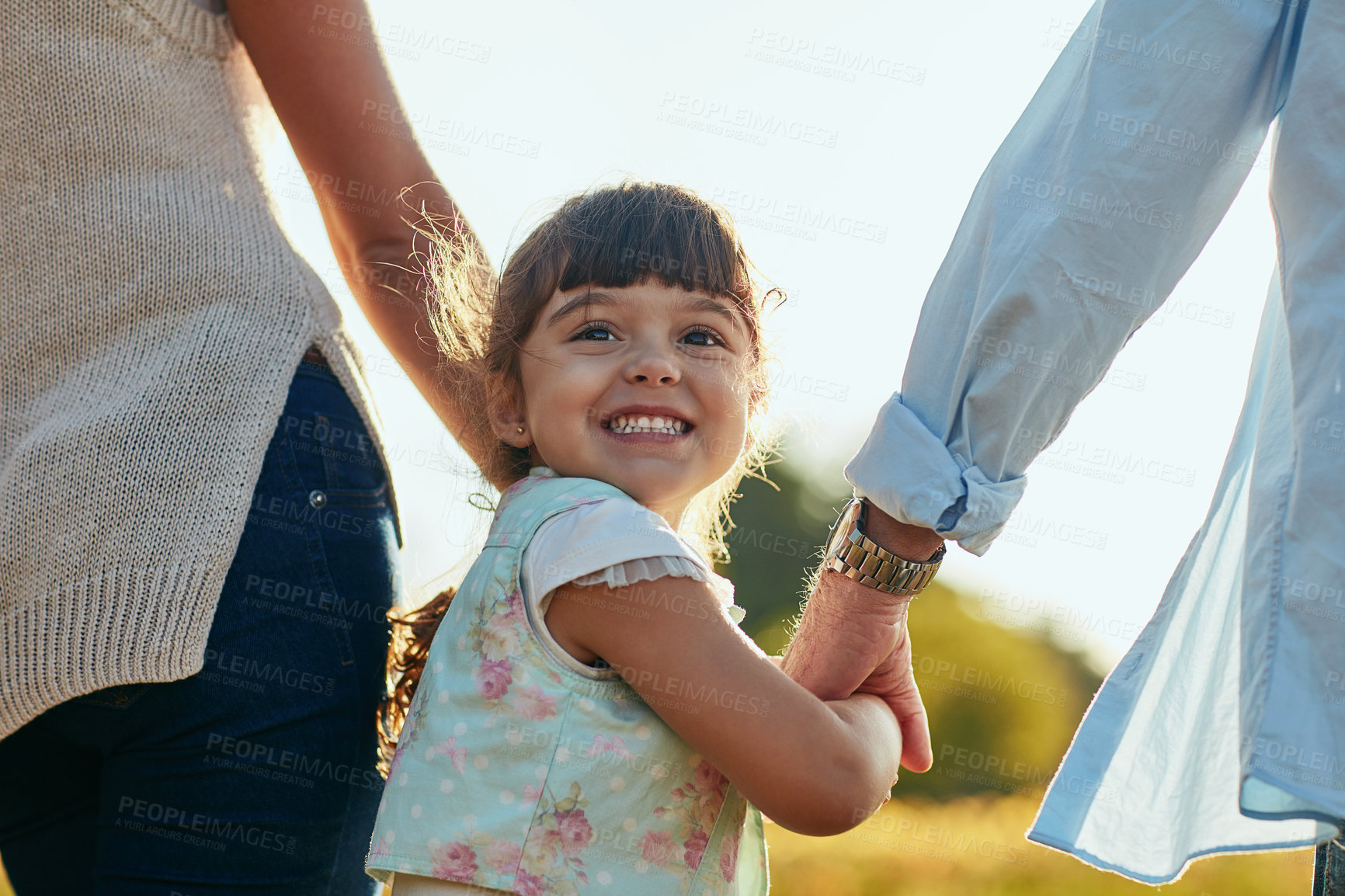 Buy stock photo Portrait of an adorable and happy little girl holding her mother and father’s hands in the park