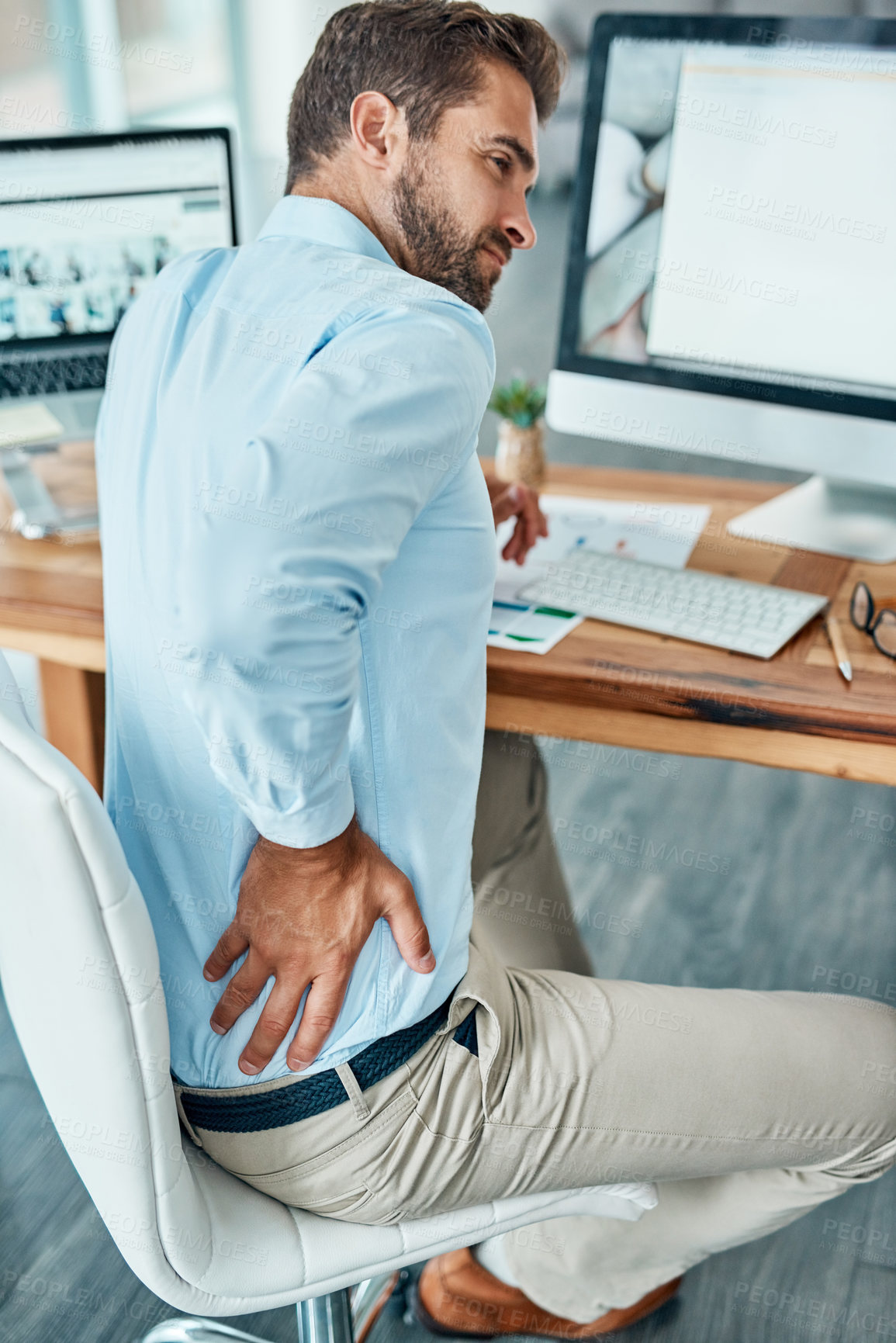 Buy stock photo Shot of a young businessman suffering with back pain while working in an office