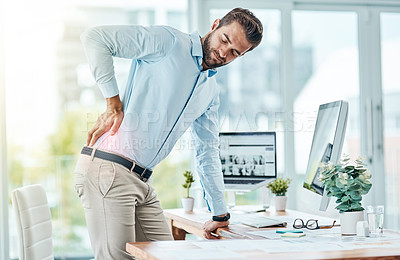 Buy stock photo Shot of a young businessman suffering with back pain while working in an office