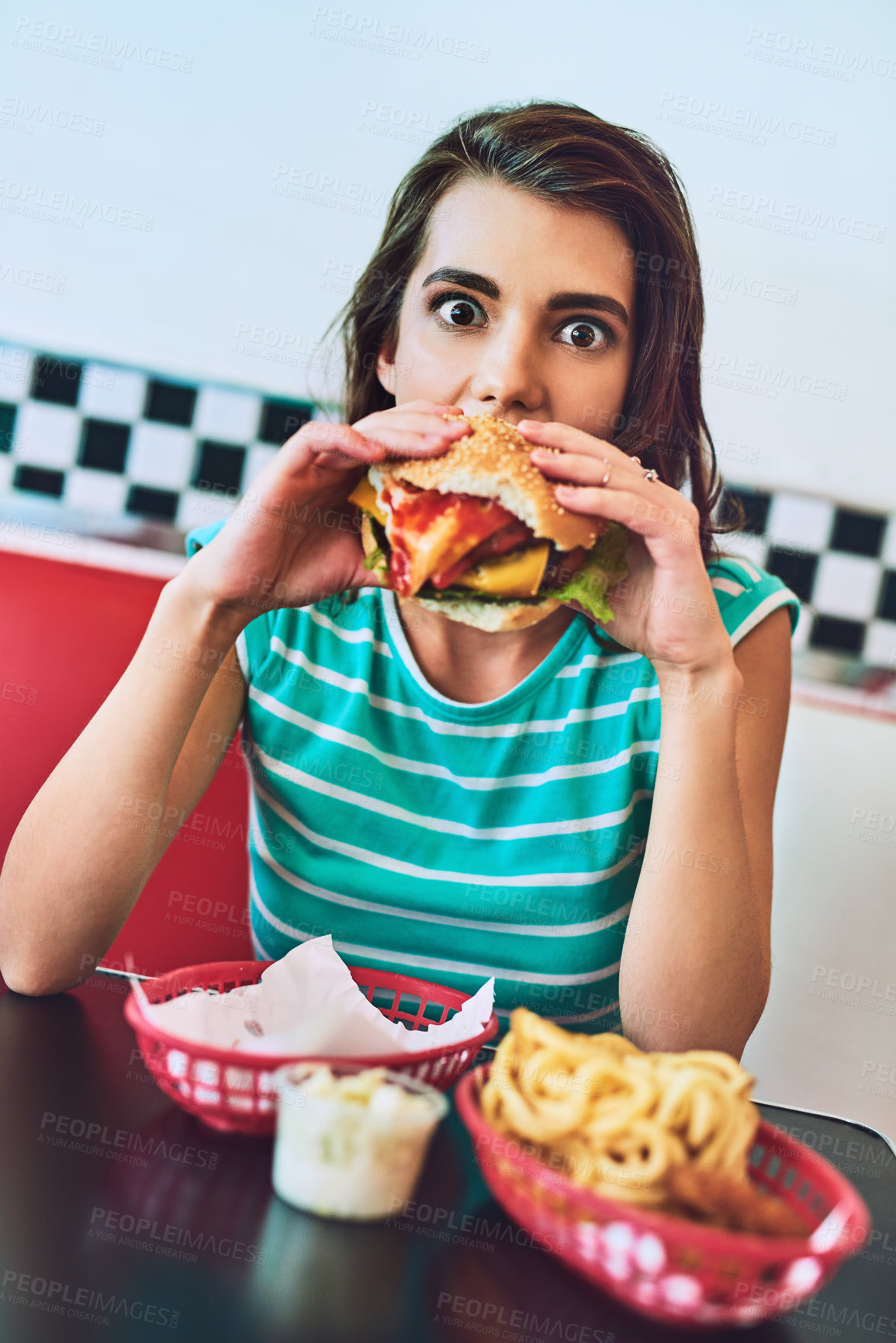 Buy stock photo Cropped portrait of an attractive young woman enjoying a burger in a retro diner