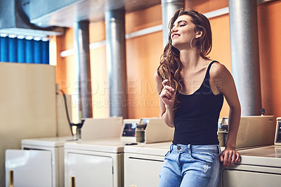 Buy stock photo Shot of an attractive young woman standing in a laundry room while waiting for washing to be done during the day