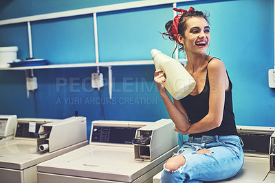Buy stock photo Shot of an attractive young woman seated on a washing machine while holding bleach to wash her washing with inside of a laundry room during the day