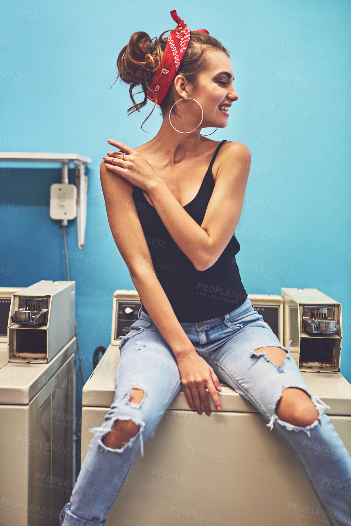 Buy stock photo Shot of an attractive young woman seated on a washing machine while waiting for the washing to be washed inside of a laundry room