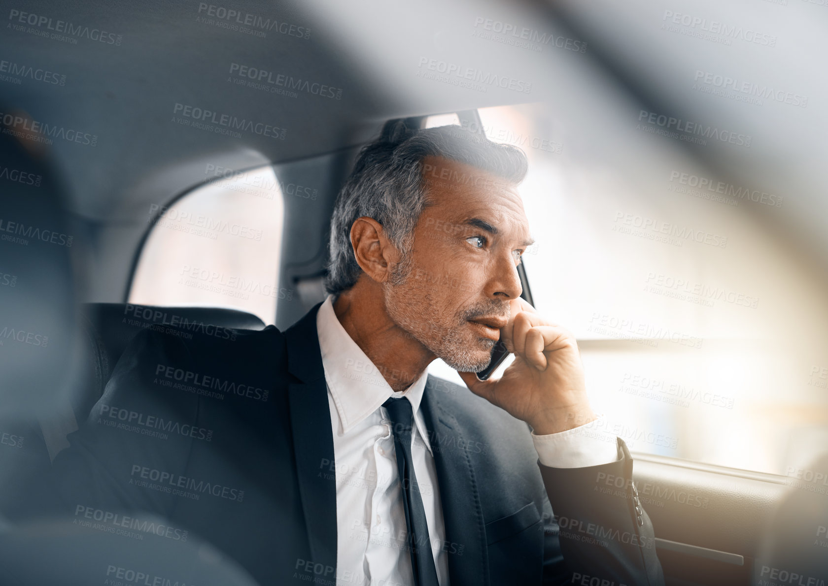 Buy stock photo Cropped shot of a handsome mature businessman making a call from the backseat of a car during his morning commute