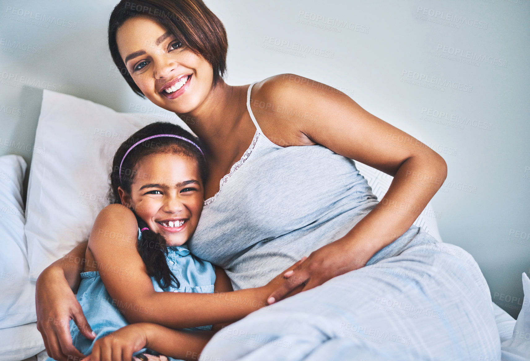 Buy stock photo Portrait of a cheerful little girl relaxing on the bed with her pregnant mother at home during the day