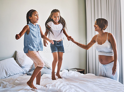 Buy stock photo Shot of a cheerful young family jumping around on a bed together at home during the day
