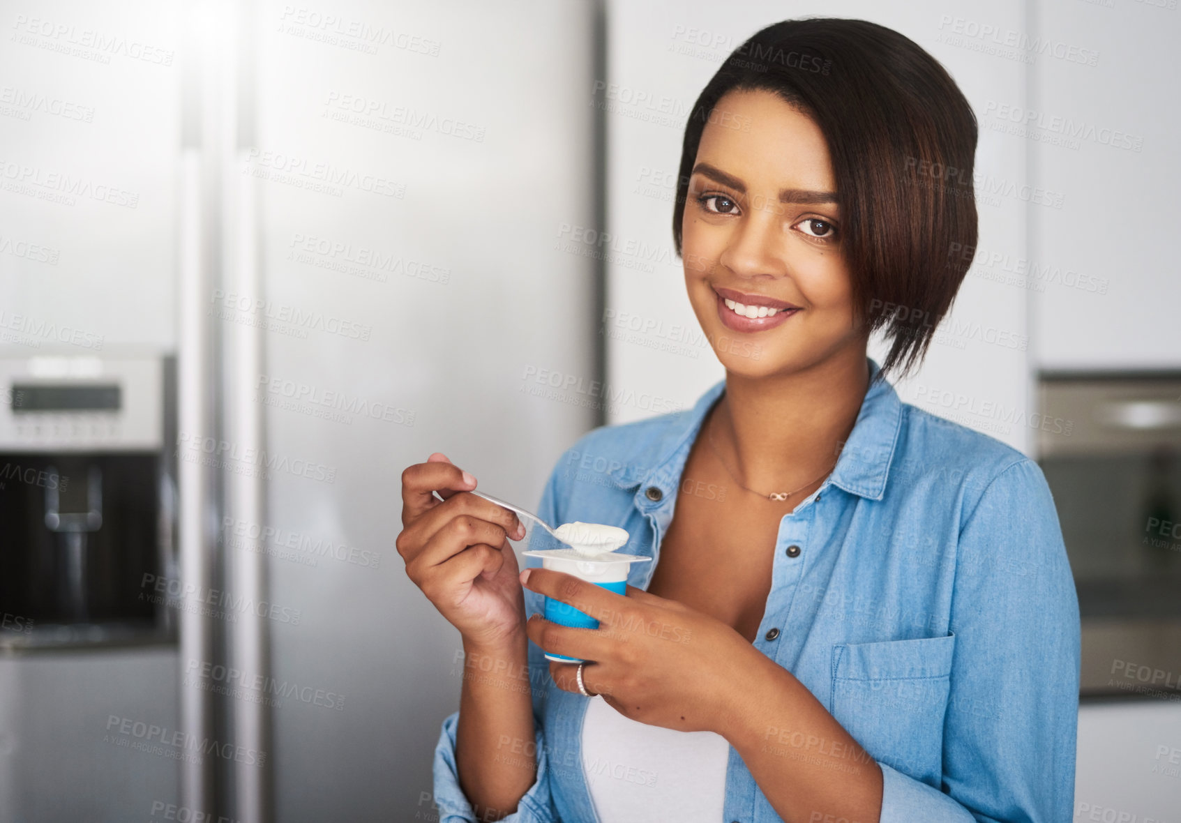 Buy stock photo Shot of an attractive young woman eating a tub of yoghurt at home